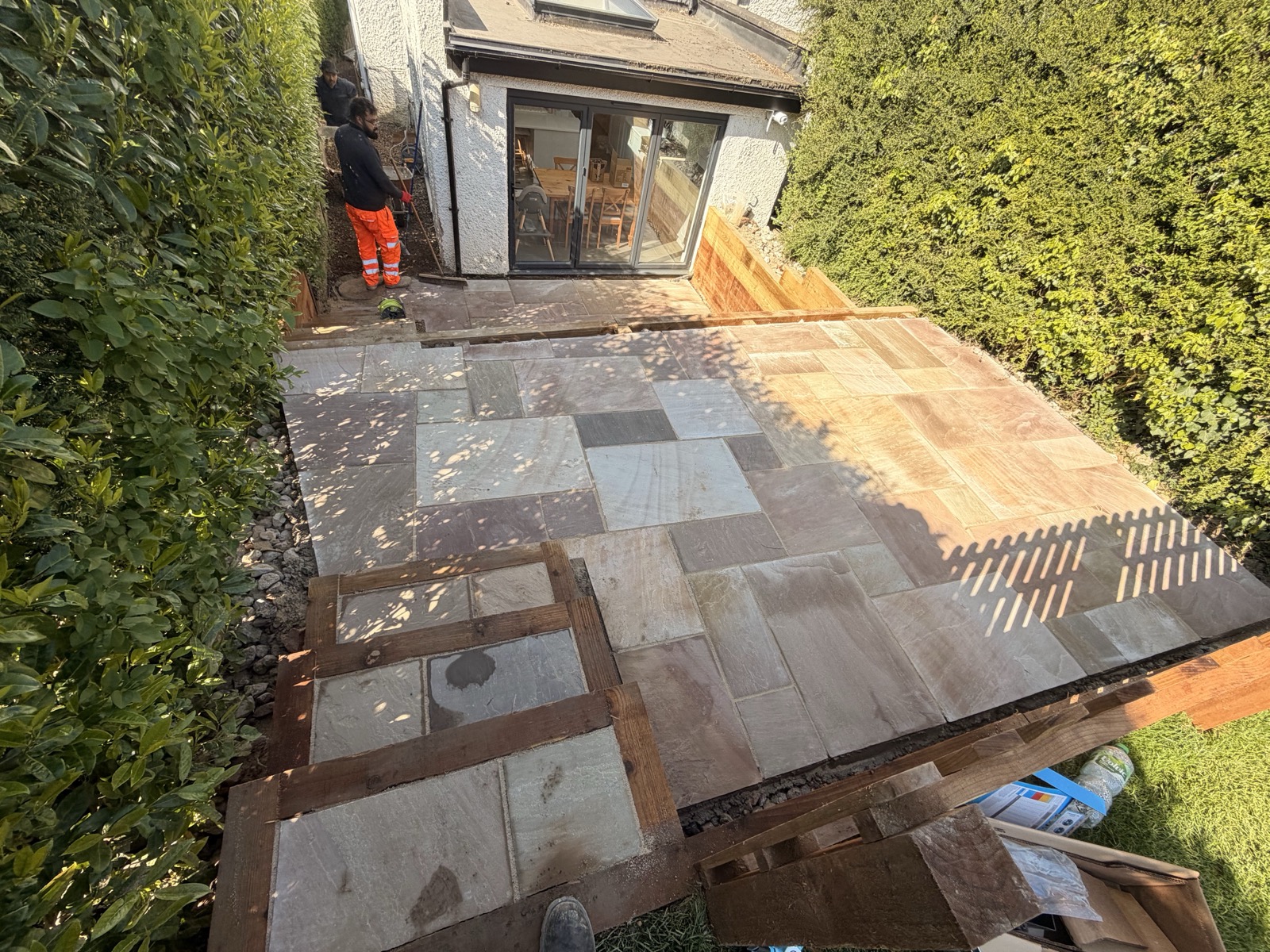 A sandstone patio mid-installation — slabs bedded and laid to falls across a levelled base, the stage where most of the real work is done before it shows.
